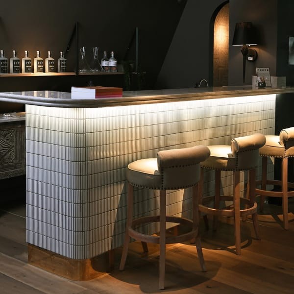 Mayfair bar stool with a low backrest, linen upholstery and wooden legs, ideal for kitchen islands and bar counters.