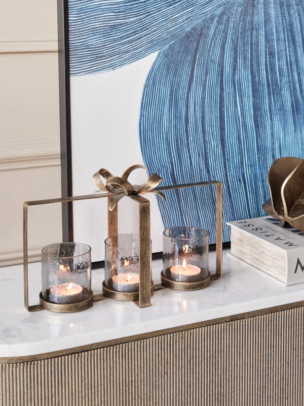Bow gold candle holder styled on a console with lit candles