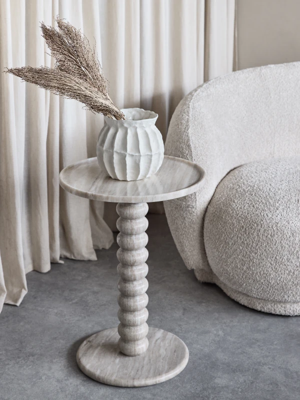 Venice beige marble side table beside a cream armchair